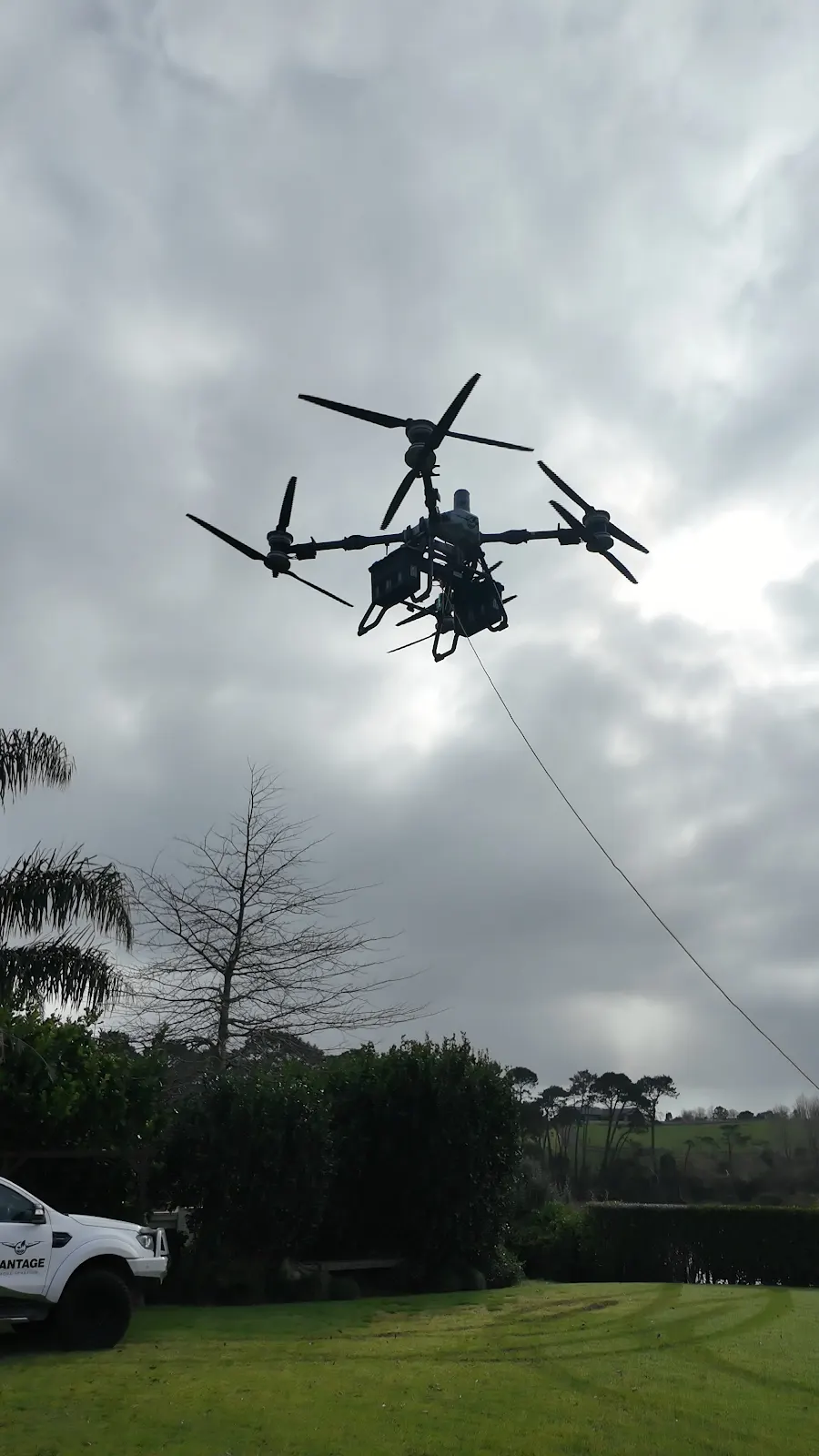 DJI Agras T100 heavy-lift drone flying above Riverhead Tavern with lifting line deployed